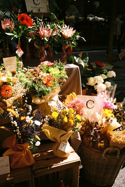 An assortment of freshly arranged floral bouquets displayed on a wooden table, featuring a variety of flowers including pink lilies, red gerbera daisies, and white baby's breath, wrapped in brown craf