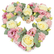 A densely flowered heart-shaped wreath fills the frame, standing out clearly against a bright white background, its pastel colours and textured petals creating a serene, comforting presence. At the foundation of this tribute are large, creamy ivory and pale yellow roses, their layered petals spiralling inward to form classic, full blooms that set a tone of quiet elegance. Around and between them, soft pink carnations cluster in abundance, their ruffled edges overlapping to form a gentle, billowing surface that softens every line of the heart. Deeper rose-pink to mauve lisianthus blooms are placed thoughtfully throughout, their open, cup-like shapes and subtle shading lending depth and emotion, much like the changing light over the rooftops of St Paul's Cray on a still evening. Silver-green eucalyptus threads through the entire composition, its rounded leaves adding a cool, calming contrast and defining the curve of the heart with natural grace. Tiny yellow-green buds push through the petals here and there, hinting at new beginnings and the freshness of flowers gathered locally and arranged with care that same day. The design feels plush and abundant, with no empty spaces, yet the delicate palette of pinks, creams, and greens keeps it gentle and soothing. This heart wreath would be a poignant choice for a funeral, cremation, or memorial service in St Paul's Cray, conveying enduring love, respect, and remembrance, and offering a soft visual focus for family and friends as they gather to say their last goodbyes.